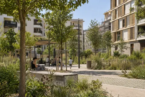 Quartier de logements sociaux rénové avec arbres, ombrage et espaces publics adaptés aux canicules
